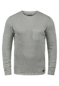 Grauer, gerippter Strickpullover mit langen Ärmeln und rundem Ausschnitt, ausgestattet mit einer Brusttasche und einem kleinen braunen Etikett am Saum.