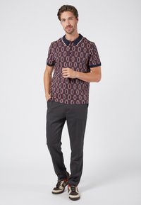Polo azul con estampado de diamantes, de mangas cortas y con un cuello en contraste; combinado con pantalones oscuros y zapatillas casuales.