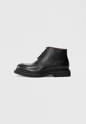 Must musta ankle saapad, lace-up kinnitusega, ümaral toe ja paksul kummist tallal, valge tausta ees.