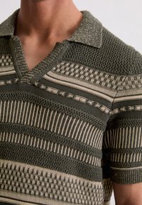 Gebreide poloshirt in donker groen en beige tinten. Kenmerken zijn afwisselende gestructureerde strepen en een geribde kraag. Korte mouwen.