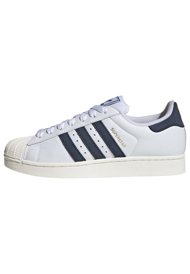 White Adidas Superstar sneaker with black stripes, shell toe, and "Superstar" label on the side.