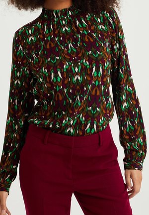 Blusa multicolore con collo alto, maniche lunghe e un vivace motivo astratto con tonalità di verde, marrone, bordeaux e bianco.