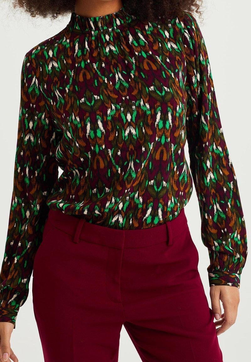 Färgglad blus med hög hals, långa ärmar och ett livligt abstrakt mönster i gröna, vinröda, bruna och vita nyanser.