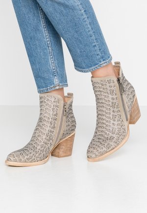 Ankelhøje beige støvler med blokhæle, sideselåse og glitrende pynt, brugt med blå denimjeans.