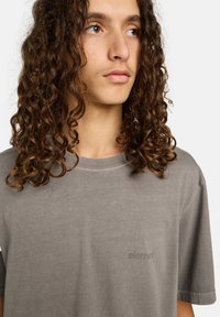 Szara bawełniana koszulka z krótkimi rękawami, z okrągłym dekoldem i małym, subtelnym logo na piersi. Gładka tekstura.