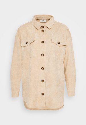 Veste chemise en velours côtelé beige avec un col, fermeture par boutons sur le devant, deux poches poitrine et une coupe décontractée. Tissu texturé avec des côtes verticales.