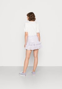 Camiseta branca de manga curta com acabamento em renda, combinada com uma saia lilás com estampado floral e bainha com babados. Ténis lavanda completam o look.