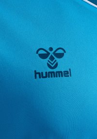 Niebieska tkanina sportowa z ciemnoniebieskim logo hummel, składającym się ze stylizowanej pszczoły i nazwy marki poniżej środka.