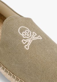 Grøn canvas slip-on sko med et broderet skull and crossbones i hvid. Sålen er lavet af jute med en syet kant.