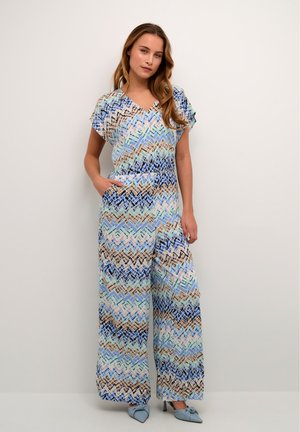 Jumpsuit a fantasia con maniche corte, scollo a V e tasche. Presenta un design geometrico nei colori blu, beige e pastello. Vestibilità morbida.