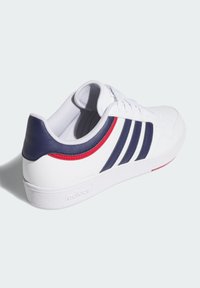 Białe sneakersy z granatowymi i czerwonymi akcentami, z trzema bocznymi paskami, teksturowanym skórzanym obcasem i płaską białą gumową podeszwą.