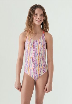 Ragazza giovane con capelli mossi che indossa un costume intero con righe astratte verticali multicolori su sfondo chiaro.