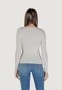 Top bianco a maniche lunghe con scollo rotondo, abbinato a jeans in denim blu chiaro con tasche posteriori e un motivo sottile.