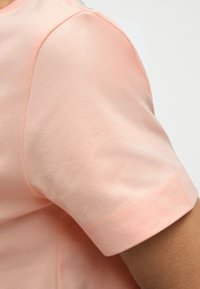 Κοντινό πλάνο στο πάνω μέρος του χεριού ενός ατόμου που φοράει ανοιχτό ροζ κοντομάνικο πουκάμισο, με λευκό φόντο.