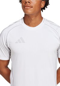 T-shirt atletico bianco a maniche corte, con colletto a costine e sottili cuciture grigie sulle spalle, caratterizzato da un logo grigio minimalista sul petto.