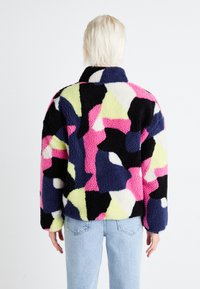 Kurtka polarowa z abstrakcyjnym wzorem w kolorach czarnym, różowym, granatowym i limonkowym. Posiada wysoki kołnierz, długie rękawy oraz miękką fakturę.