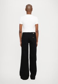 Black wide-leg pants made of denim feature a rear logo patch and back pockets. Paired with a plain white short-sleeve T-shirt.