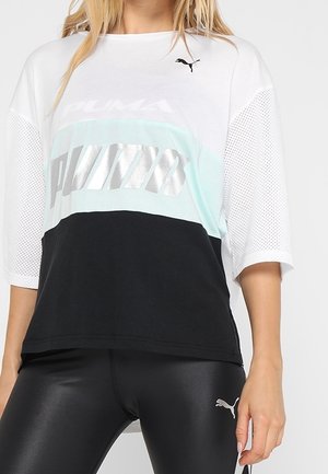 Mujer con una camiseta blanca y negra de Puma con mangas de malla y mallas negras brillantes de Puma.