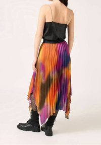 Färgglad veckad kjol med asymmetrisk nederkant, i orange, lila och svarta nyanser, tillsammans med en svart satin topp och kraftiga svarta stövlar.