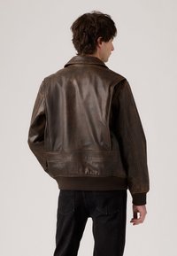 Brown leather bomber jacket with a smooth texture, featuring ribbed cuffs and hem, shoulder seams, and a classic collar design.