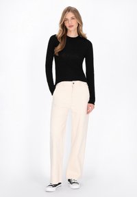 Zwart langemouw top gecombineerd met lichtbeige wijde broek en zwarte sneakers. De broek heeft twee frontzakken en een knoopsluiting.