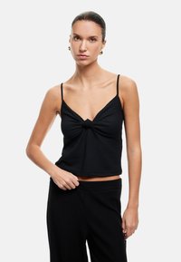 Top negro de canalé con un centro anudado, tirantes finos y una silueta fluida, combinado con pantalones negros de talle alto a juego.