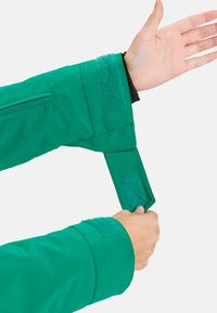 Groene jacksleeve met verstelbare klittenbandmanchet. Glad stof met een verborgen ritsvak en versterkte stiksels.