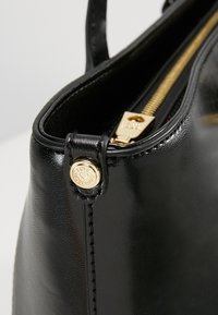 Black leather handbag featuring a shiny finish, gold hardware, a zip closure, and a logo accent on a snap button. Smooth texture and structured shape.