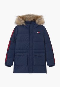 Námorně modrá péřová bunda s kapucí lemovanou kožešinou, červené logo "Tommy Hilfiger" na rukávech, dvě přední kapsy s klopou a malá náprsní nášivka.