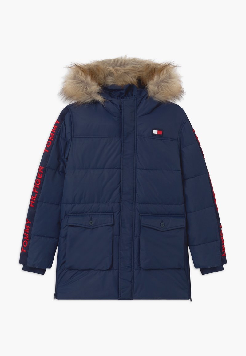 Námorně modrá péřová bunda s kapucí lemovanou kožešinou, červené logo "Tommy Hilfiger" na rukávech, dvě přední kapsy s klopou a malá náprsní nášivka.