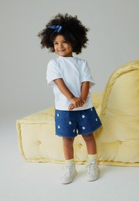 Wit T-shirt met korte mouwen, denim shorts met witte bloemenborduursels, gegolfde zoom, gecombineerd met witte hoge sneakers en gele sokken.