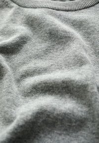 Miękka, szara dzianina z delikatnym ściegiem i subtelnymi fałdami podkreślającymi fakturę oraz szczegóły materiału.