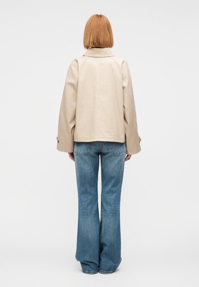 Μπεζ κοντό μπουφά ν με φαρδιά μανίκια και γιακά με σχισμές. Συνδυάζεται με καμπάνα ανοιχτό μπλε τζιν, με ξεθωριασμένη υφή ντένιμ.