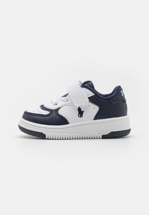 Børns sporty sneakers i navyblå og hvid med velcrolukning, snøreudsnit og Polo-logo på siden og hælen, på en ensfarvet baggrund.
