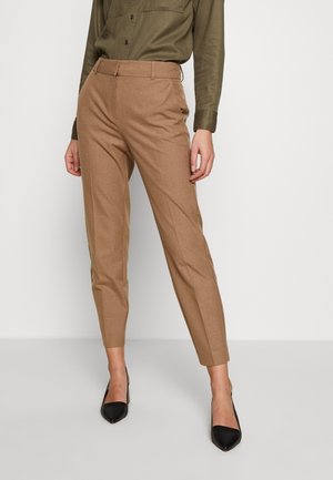 Pantalons taillés beiges en tissu texturé, avec une coupe slim, un devant plat et des poches latérales, associés à des chaussures noires à talons pointus.