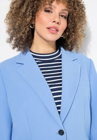 Blazer bleu clair avec un col cranté, un bouton noir unique et une poche plaquée, superposé à un haut rayé bleu marine et blanc.