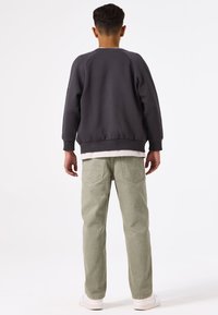 Sudadera gris con cuello redondo y puños acanalados, combinada con pantalones rectos de color verde claro, llevada con zapatillas blancas.