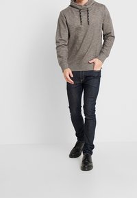 Grå hætte sweatshirt med en struktureret overflade, parret med mørkeblå slim-fit jeans og sorte snørebåndssko.