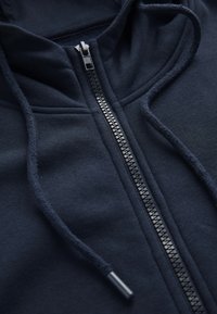 Marinblå zip-up hoodie med en slät tygtextur, justerbara dragsko, och en kontrasterande dragkedja som går ner fram.