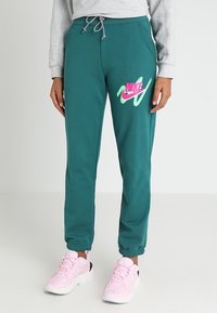 Teal sweatpants har en elastisk midja med dragsko, elastiska muddar och en rosa Nike-logotyp med gröna accenter på vänster lår.