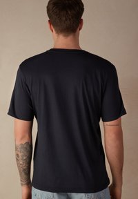 Námorně modré tričko s krátkým rukávem a volným střihem. Obsahuje kulatý výstřih a hladkou bavlněnou tkaninu. Viditelné tetování na levém rameni.