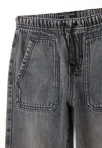 Joggers de mezclilla gris con cintura elástica, cierre de cordón y dos bolsillos grandes con detalles de costura.