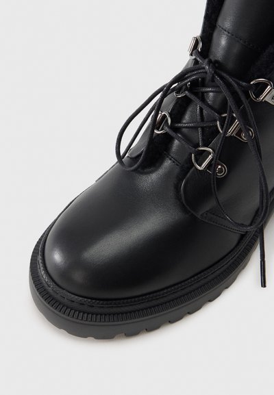 Czarny skórzany botek za kostkę z zaokrąglonym noskiem, teksturowaną podeszwą i metalowymi oczkami na sznurowadła. Posiada miękkie wnętrze i sznurowany fason.