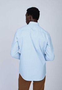 Chemise à manches longues de couleur bleu clair avec un col boutonné. Présente un motif géométrique subtil et un ourlet arrondi.
