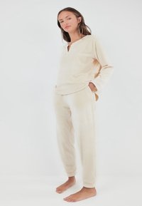Ensemble de détente beige clair en tissu doux, comprenant un haut à manches longues avec un décolleté en V et un pantalon assorti avec des bords-côtes, tous deux ornés de points subtils.