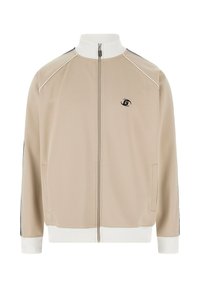 Beige trainingsjack met een hoge witte kraag, een ritssluiting aan de voorkant, zijzakken en zwarte accenten op de mouwen. Heeft een klein logo op de borst.