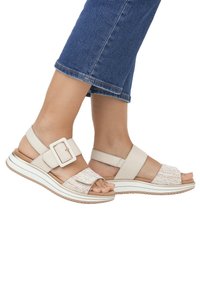 Sandali beige con cinturini intrecciati texturizzati, grande dettaglio della fibbia e suola a piattaforma con strisce bianche e marroni.