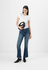 Chemise blanche à manches courtes, jean bleu évasé, sac à main noir et bottes à talons hauts noires. Tissu lisse et texture en denim classique.