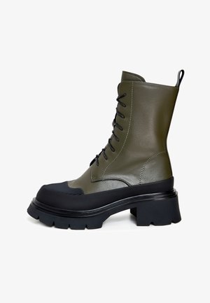 Stivale alla caviglia verde oliva con lacci, finitura lucida, punta in gomma, tacco chunky nero e suola texturizzata.