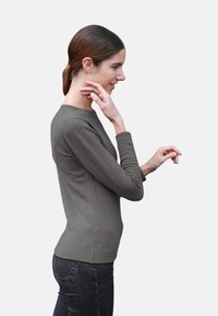 Haut à manches longues de couleur vert olive en tissu doux, doté d'un col rond et d'une coupe ajustée, associé à un jean foncé.